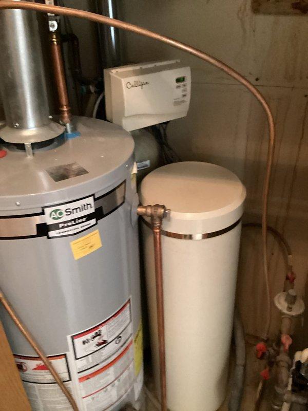 Conducted on-site assessment of basement water heating and treatment system in preparation for utility company water meter replacement. Evaluated A.O. Smith tanked water heater and adjacent water softener system to determine scope of work required for temporary relocation. Assessment identified need to relocate T&P valve on water heater and reposition water softener salt tank to provide access for RPU meter installation. Documented existing equipment configuration including copper piping connections between water heater and softener system, wall-mounted control panel, and plumbing fixture locations. Prepared estimate for two-phase service: initial removal and relocation of salt tank and T&P valve modification to accommodate meter changeout, followed by return visit to reinstall salt tank and restore system to operational status. Photographed current installation showing equipment placement, piping layout, and access constraints in utility area.