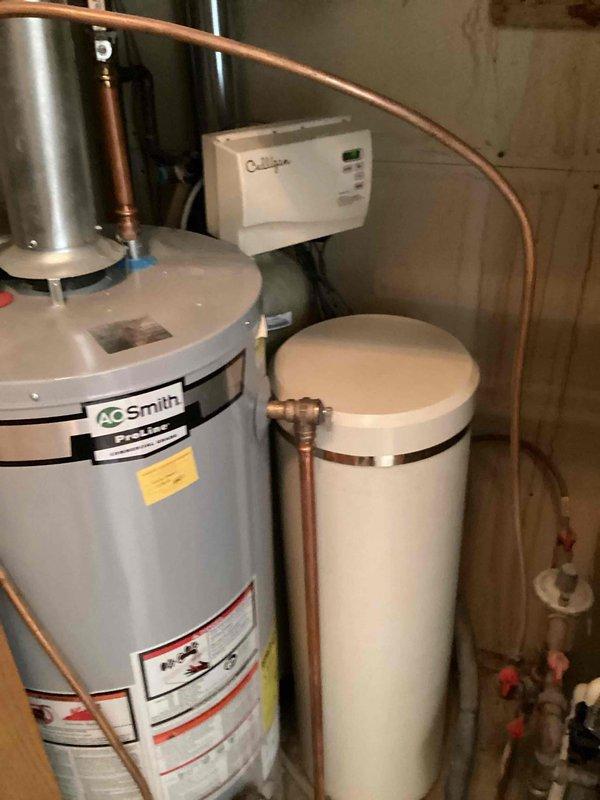 Conducted on-site assessment of basement water heating and treatment system in preparation for utility company water meter replacement. Evaluated A.O. Smith tanked water heater and adjacent water softener system to determine scope of work required for temporary relocation. Assessment identified need to relocate T&P valve on water heater and reposition water softener salt tank to provide access for RPU meter installation. Documented existing equipment configuration including copper piping connections between water heater and softener system, wall-mounted control panel, and plumbing fixture locations. Prepared estimate for two-phase service: initial removal and relocation of salt tank and T&P valve modification to accommodate meter changeout, followed by return visit to reinstall salt tank and restore system to operational status. Photographed current installation showing equipment placement, piping layout, and access constraints in utility area.