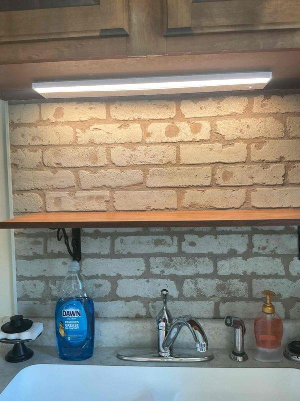 Responded to service call for non-functional light fixture above kitchen sink. Upon arrival, diagnosed failed under-cabinet fluorescent light fixture in kitchen workspace with exposed brick backsplash. Removed old fluorescent fixture and replaced with new LED under-cabinet lighting unit to provide improved illumination for sink area. Verified proper operation of new LED fixture and restored lighting functionality to workspace.