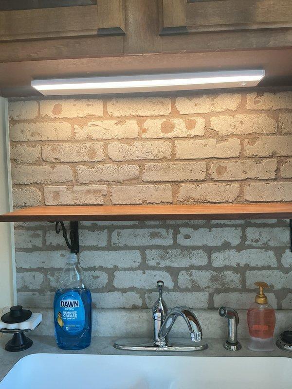 Responded to service call for non-functional light fixture above kitchen sink. Upon arrival, diagnosed failed under-cabinet fluorescent light fixture in kitchen workspace with exposed brick backsplash. Removed old fluorescent fixture and replaced with new LED under-cabinet lighting unit to provide improved illumination for sink area. Verified proper operation of new LED fixture and restored lighting functionality to workspace.