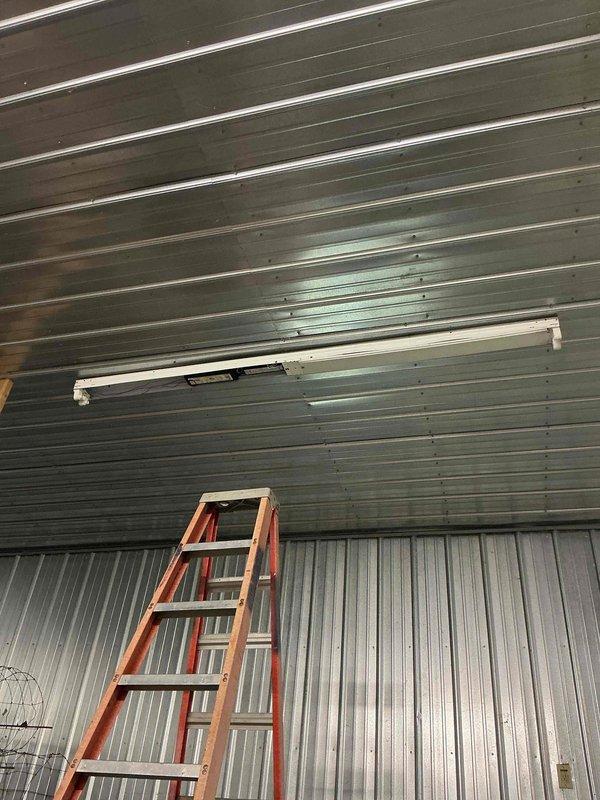 Completed electrical work on white metal shed building that was started a year prior. Diagnosed and replaced failed ballasts in two fluorescent light fixtures mounted on the corrugated metal ceiling. Both fixtures are now operational and providing proper illumination to the interior space.