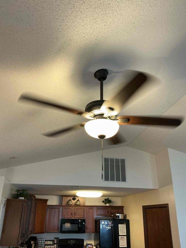 Installed customer-supplied ceiling fan with integrated light fixture in residential kitchen area, mounting unit to vaulted ceiling via downrod assembly. Verified proper electrical connections, tested fan operation across all speed settings and light functionality, and confirmed secure installation with pull chain controls operational.