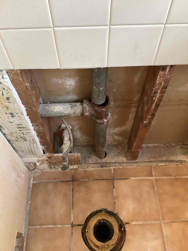 Responded to upstairs bathroom vanity sink draining into basement bathroom. Created wall access to inspect drainage system and discovered 1-1/2" galvanized lavatory drain had separated at the tee fitting inside the wall cavity. Upon further investigation, found extensive buildup throughout the drain line preventing proper drainage. Documented conditions showing corroded galvanized piping, deteriorated fittings, and significant moisture damage to surrounding wall framing. Advised that drain line requires hydro jetting service to remove blockages and restore proper flow before reassembly can be completed.
