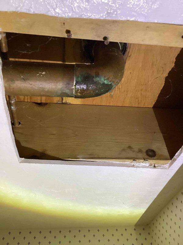 Responded to water line leak originating from shower valve in upstairs bathroom. Previous visit was unable to access leak due to mold obstruction; upon return, mold had been remediated providing clear access to plumbing system. Investigation revealed leak coming from one of two back-to-back shower valves with limited access to water lines through ceiling cavity. Accessed leak location through ceiling opening, exposing copper supply lines running through floor joists. Identified corroded copper piping with visible green patina at valve connection point as source of active leak. Documented existing conditions including water damage, compromised drywall, and plumbing configuration. Assessed repair options given challenging access constraints with back-to-back shower installations and lack of direct wall access to water lines. Provided recommendations for permanent repair solutions including potential rerouting of supply lines or creation of access panel for future serviceability.