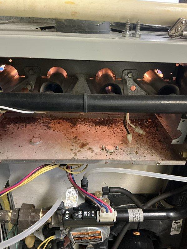 Responded to service call for furnace with reported water leakage issues ongoing since previous no-cooling call. Upon arrival, found standing water on ground near unit and confirmed active condensate leak causing extensive corrosion throughout system. Inspection revealed severely deteriorated burner assemblies, heavy rust accumulation on heat exchanger panels and base platform, and significant corrosion on internal metal surfaces and electrical components including control boards. Documented extensive damage with photographs showing compromised burners, corroded metal housing, rust-covered base pan, and deteriorated electrical control area. Due to advanced age of equipment and extent of water damage affecting critical components including heat exchanger, burners, and control systems, recommended full system replacement as most cost-effective solution. Provided repair and replacement options to address safety concerns and system reliability issues.