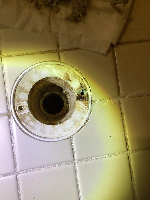 Responded to a slow-draining, backed-up master shower drain. Removed the strainer cover and found heavy mineral scale buildup and hair debris restricting the drain line. Cleared the scale and debris from the line, restoring full drainage, and noted corrosion and a cracked flange at the drain opening.