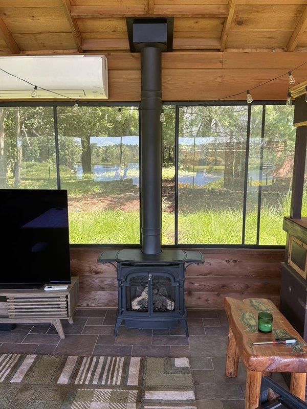 Responded to service call for non-operational outdoor fireplace located in screened porch area. Upon arrival, inspected wood-burning stove installation and surrounding components. Examined gas fire pit assembly with decorative lava rock arrangement and identified issues with burner system components including damaged or improperly configured gas supply fittings visible in metal basket assembly. Assessed venting system, stovepipe installation, and clearances to combustible materials. Documented existing conditions with photographs for follow-up service requirements.