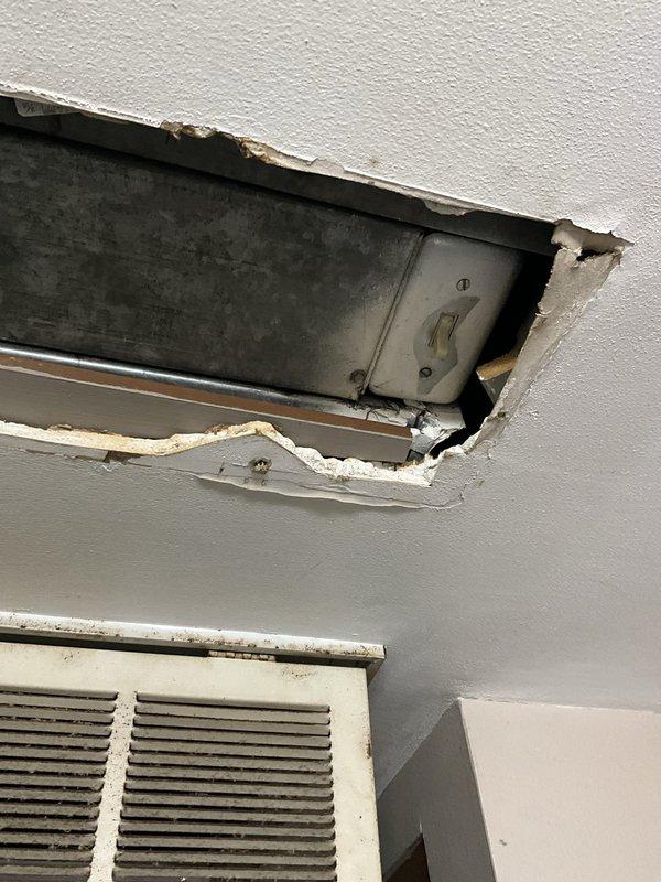 Performed comprehensive assessment of non-operational air conditioning system located in ceiling void between bathroom and bedroom. Unit has history of capacitor replacement and previous refrigerant leak issues. Property utilizes baseboard heating with dual thermostat configuration in living area controlling separate heating and cooling systems. Documented existing equipment conditions including corroded exterior electrical connections and damaged interior wall access panel near cooling system location. Provided replacement estimate for complete AC system due to age, recurring component failures, and compromised refrigerant integrity.