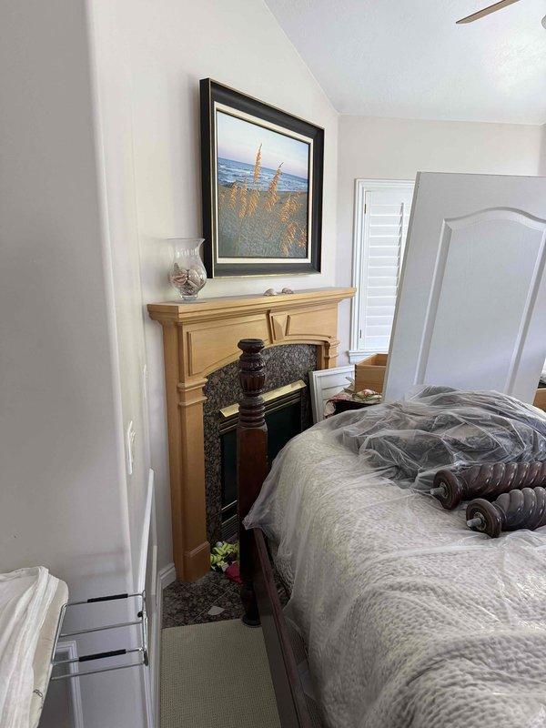 Conducted on-site evaluation of existing see-through fireplace unit for replacement estimate. Documented current installation featuring light wood mantel surround with granite aggregate facing and dark glass-fronted firebox visible from both bedroom and living room sides. Photographed both viewing areas to capture existing mantel configurations, clearances, and surrounding finishes including carpeted and hardwood flooring. Assessed structural opening dimensions and venting requirements for replacement unit specifications. Customer seeking updated see-through fireplace model with similar functionality to maintain dual-room viewing capability.