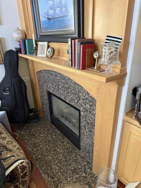 Conducted on-site evaluation of existing see-through fireplace unit for replacement estimate. Documented current installation featuring light wood mantel surround with granite aggregate facing and dark glass-fronted firebox visible from both bedroom and living room sides. Photographed both viewing areas to capture existing mantel configurations, clearances, and surrounding finishes including carpeted and hardwood flooring. Assessed structural opening dimensions and venting requirements for replacement unit specifications. Customer seeking updated see-through fireplace model with similar functionality to maintain dual-room viewing capability.