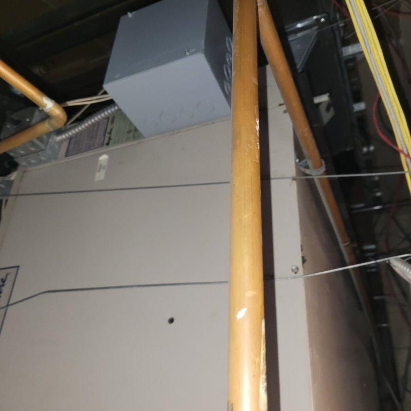 Responded to commercial facility reporting one of three ceiling-mounted AC units not producing cold air. Upon arrival, accessed approximately 20-year-old air handler unit installed in ceiling space above business location. Performed comprehensive Cool 10+ preventive maintenance inspection on the affected system. Examined air handler cabinet, refrigerant lines, and associated components in confined ceiling installation area. Inspected copper refrigerant piping, electrical connections, and control systems. Verified proper operation of all mechanical components and assessed overall system condition given age of equipment. Documented existing installation configuration with multiple copper lines running through structural framing. System evaluated for cooling performance and operational efficiency to address reported lack of cold air output.