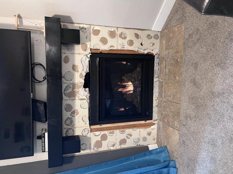 Completed installation of BX36NTRE fireplace unit with PRPB36 components, utilizing access code 7449# for system configuration. Unit installed with black-framed glass door, river rock decorative surround, and wooden mantel, verified proper ignition and flame operation, and documented completed installation with photos showing functional fireplace in residential living space.