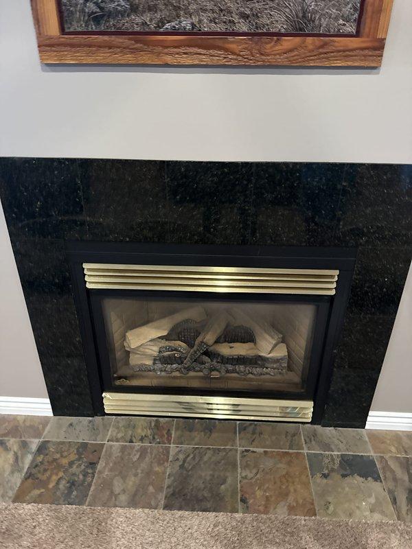 Conducted comprehensive fireplace replacement estimate for 26-year-old gas fireplace unit located on main floor. Evaluated existing installation featuring black speckled granite surround, brass trim, and slate hearth with current vented gas log system. Assessed exterior termination point through brick wall, noting existing vent hood condition and clearances. Provided technical specifications and recommendations for BX42 model replacement unit, including necessary modifications to existing surround, venting requirements, and compatibility with current installation footprint.