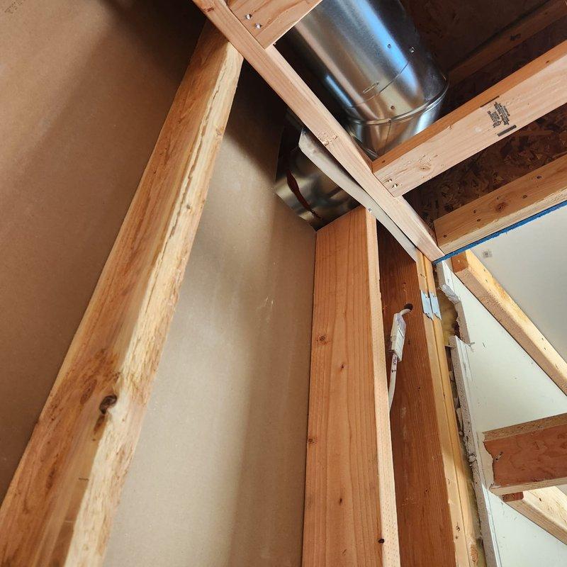 Responded to callback for failed fireplace inspection requiring multiple code compliance corrections. Documented existing deficiencies including missing fire caulk at penetrations, inadequate strapping, gaps around flue penetrations, wiring positioned too close to flue pipe, and compromised roof flashing with small holes. Photographed unfinished attic space showing HVAC ductwork installation area and structural framing where fireplace system penetrates ceiling, capturing evidence of code violations for contractor reference and subsequent remediation work.