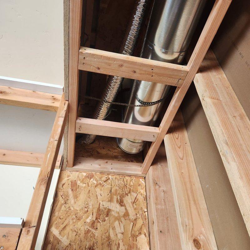 Responded to callback for failed fireplace inspection requiring multiple code compliance corrections. Documented existing deficiencies including missing fire caulk at penetrations, inadequate strapping, gaps around flue penetrations, wiring positioned too close to flue pipe, and compromised roof flashing with small holes. Photographed unfinished attic space showing HVAC ductwork installation area and structural framing where fireplace system penetrates ceiling, capturing evidence of code violations for contractor reference and subsequent remediation work.