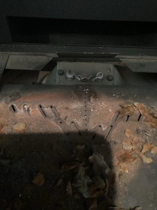 Responded to service call for 16-year-old gas fireplace experiencing intermittent cycling issues, with unit running continuously at times or shutting off after approximately 30 minutes before restarting. Upon inspection, observed significant corrosion and deterioration on burner assembly and heat exchanger components, which can cause improper flame sensing and safety system malfunctions leading to erratic operation. Documented current condition of gas fireplace insert with stone surround in living room, noting the corroded burner surfaces and accumulated debris in combustion chamber that likely contribute to inconsistent flame detection and automatic shutdown cycles.