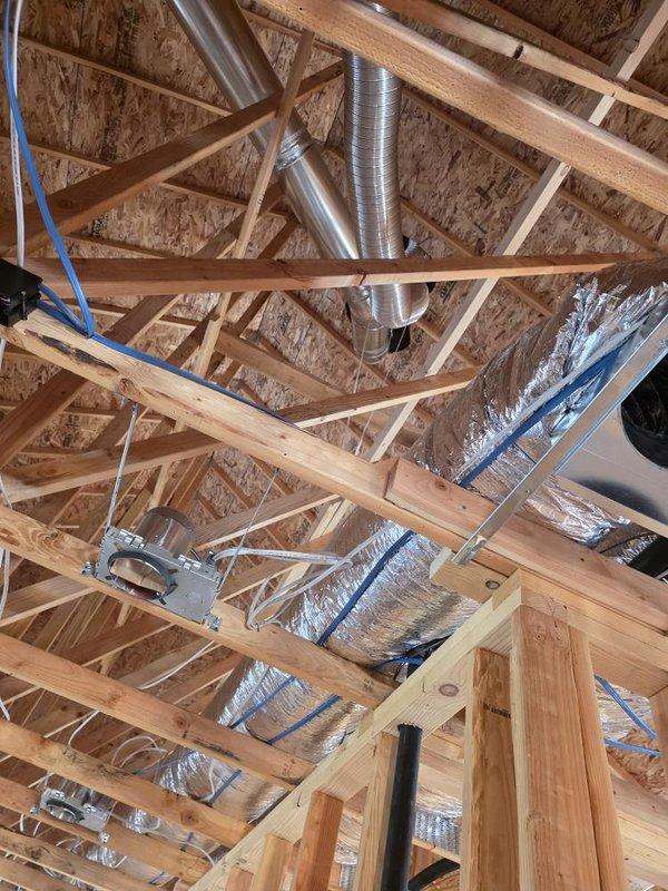 Completed fireplace installation including venting system for model AX42NTRE unit. Installed stainless steel chimney cap with flashing plate on roof, ensuring proper mounting and weatherproofing on OSB sheathing. Routed flexible aluminum ductwork through attic space, securing with metal straps and hangers to ensure proper support and clearances from roof trusses and framing members. All venting components installed to manufacturer specifications and building code requirements. Unit ready for final panel and log set installation.
