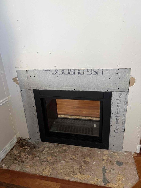 Completed QA visit for fireplace installation to verify clearance specifications for mantel and surround materials. Inspected cement board substrate installation around black metal fireplace insert and documented current construction phase with photos. Reviewed proper clearance requirements with homeowner to ensure compliance with manufacturer specifications before final finishing materials are applied.