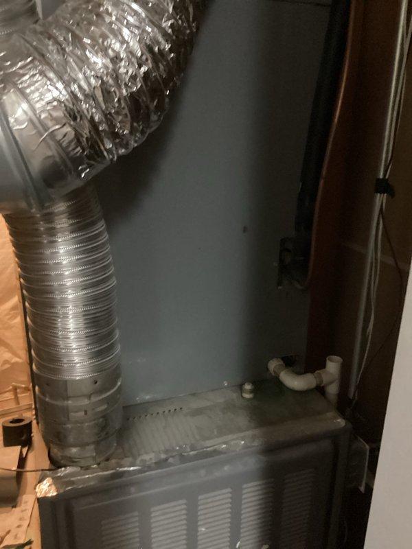 Performed an on-site evaluation for replacement of an approximately 20-year-old furnace and air conditioning system, both currently operational. Inspected the furnace cabinet in the utility closet, noting the flexible supply duct and corrugated flue connections, foil-taped surfaces, PVC condensate drain assembly, and dust and light staining on the unit. Observed aged, dusty galvanized flue and duct piping in the unfinished joist space, along with discolored joist and subfloor wood suggesting possible past moisture exposure, and documented all findings with photos to support the replacement recommendations.