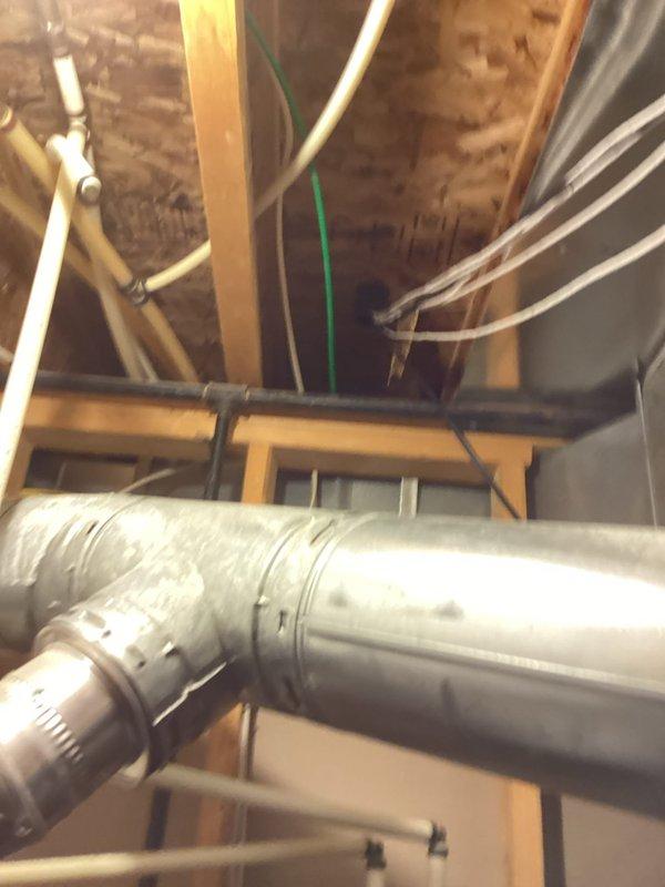 Performed an on-site evaluation for replacement of an approximately 20-year-old furnace and air conditioning system, both currently operational. Inspected the furnace cabinet in the utility closet, noting the flexible supply duct and corrugated flue connections, foil-taped surfaces, PVC condensate drain assembly, and dust and light staining on the unit. Observed aged, dusty galvanized flue and duct piping in the unfinished joist space, along with discolored joist and subfloor wood suggesting possible past moisture exposure, and documented all findings with photos to support the replacement recommendations.