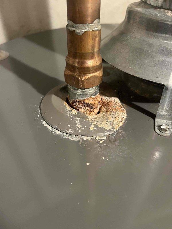 Inspected 9-year-old Rheem water heater with severely corroded fitting at the top connection point. Documented extensive deterioration where copper pipe meets brass fitting, with visible mineral deposits and rust indicating a slow leak. Provided client with repair options and replacement estimate as requested.