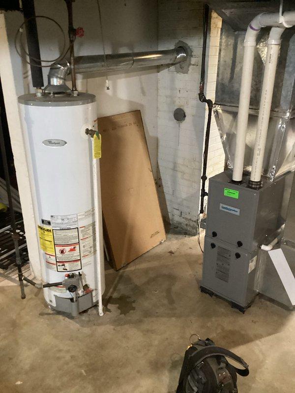 Conducted assessment for water heater replacement in 80-year-old single-family home. Existing unit located in basement utility room shows significant age with deteriorating vent piping and connection points. Documented current installation configuration including proximity to furnace and existing plumbing/ventilation setup to prepare comprehensive replacement estimate.