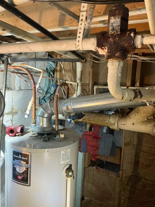 Conducted an assessment for potential installation of a combination tankless water heater/boiler system to replace existing 16-year-old boiler. Inspected current mechanical room setup, noting aging water heater with significant corrosion at pipe junctions, particularly at the iron pipe cross fitting. Documented existing HVAC ductwork configuration and plumbing connections to determine appropriate specifications for the proposed system upgrade.