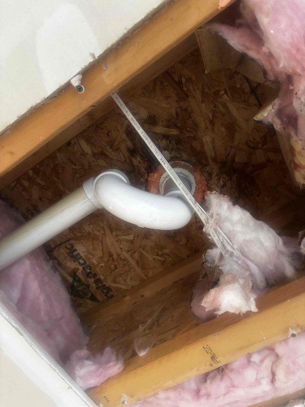 Investigated frozen bathroom pipes causing water damage to garage ceiling. Inspected drain fixture showing significant mineral buildup and discoloration. Examined wall cavity containing PVC plumbing with elbow joint, revealing inadequate insulation distribution around pipes that contributed to freezing. Resolved issue and documented with photos for service record.