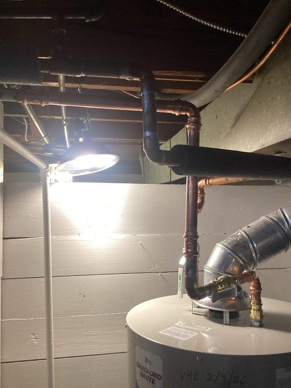 Relocated incorrectly installed cold water valve that was causing a leak in the basement plumbing system. Properly repositioned and secured the blue shut-off valve on the black pipe fittings above the copper supply lines, ensuring all connections were sealed and tested for proper function with the Bradford White water heater system.