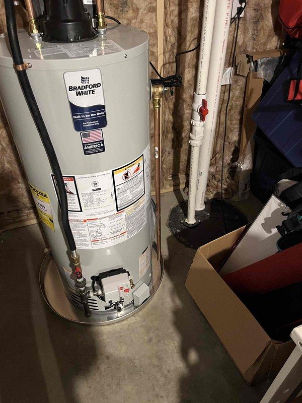 Successfully installed a Bradford White water heater in utility area, complete with all necessary connections including copper pipes with brass fittings and PVC piping. System includes a properly mounted blue expansion tank and appropriate valving, with all components verified to be in good working condition with no leaks or damage.