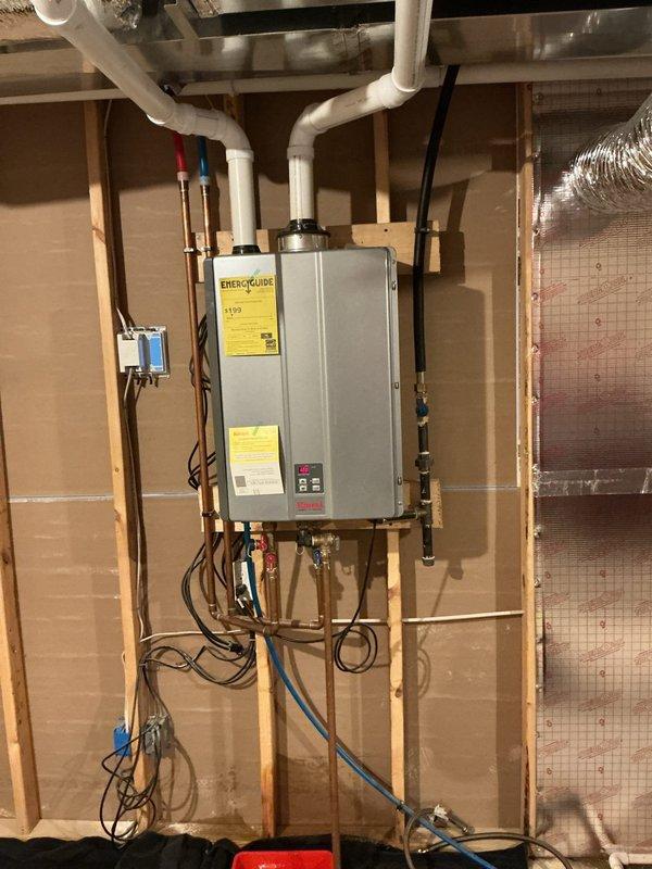 Inspected tankless water heater reported for leaking. Observed installation with proper hot/cold line connections and ventilation intact. Positioned drip bucket beneath unit and determined source of leak was from pressure relief valve connection; tightened fitting to resolve issue and verified system operation with no further leakage.