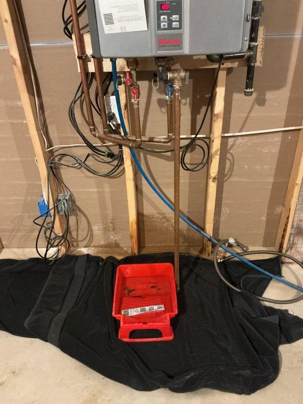 Inspected tankless water heater reported for leaking. Observed installation with proper hot/cold line connections and ventilation intact. Positioned drip bucket beneath unit and determined source of leak was from pressure relief valve connection; tightened fitting to resolve issue and verified system operation with no further leakage.