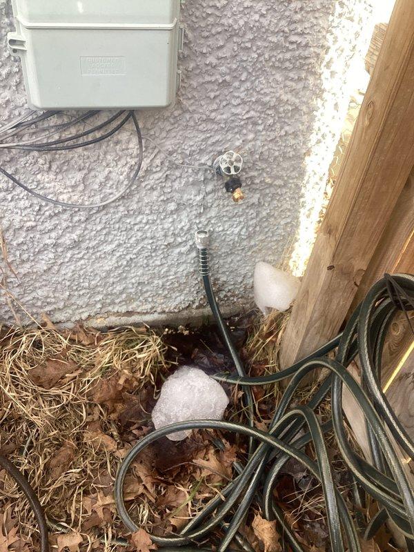 Responded to a water leak service call for a dripping outdoor spigot. Inspected the exterior wall-mounted faucet that was connected to a green garden hose and observed water accumulation with ice formation on the ground below. Verified proper operation of the building services connection and secured the fixture to prevent further leakage.