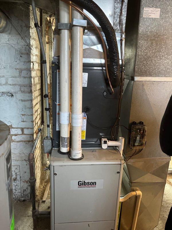 Successfully installed and replaced a residential air conditioning system including an outdoor condenser unit mounted on a concrete pad with proper line set connection and electrical disconnect box. The indoor portion of the installation included connecting the new cooling unit to the existing Gibson furnace with appropriate PVC ventilation/drainage piping and flexible ductwork in the utility area.