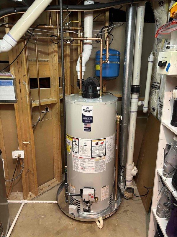 Successfully completed installation of a standard residential water heater in utility area, including proper connection of copper supply/return lines and PVC piping. Mounted blue expansion tank on wall above unit and ensured all necessary valves, fittings, and electrical connections were properly installed according to manufacturer specifications. System was tested and confirmed operational with appropriate water flow and temperature.
