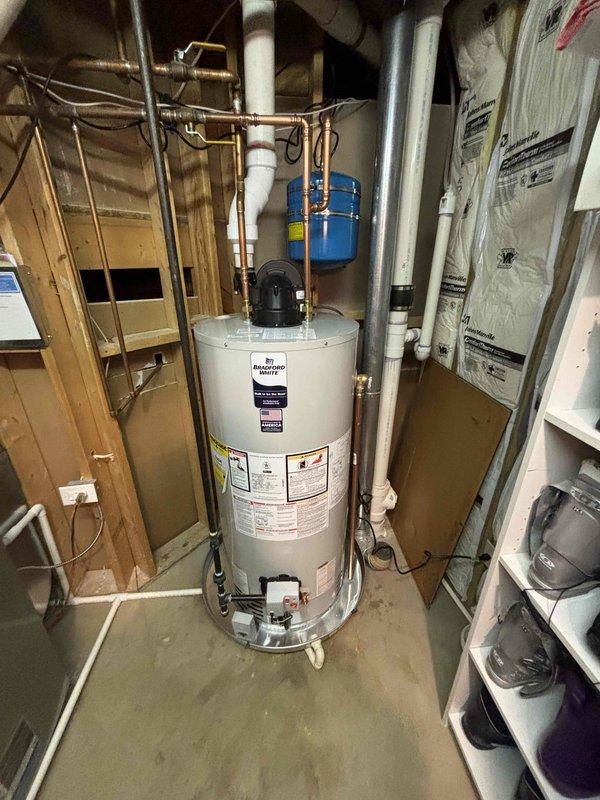 Successfully completed installation of a standard residential water heater in utility area, including proper connection of copper supply/return lines and PVC piping. Mounted blue expansion tank on wall above unit and ensured all necessary valves, fittings, and electrical connections were properly installed according to manufacturer specifications. System was tested and confirmed operational with appropriate water flow and temperature.