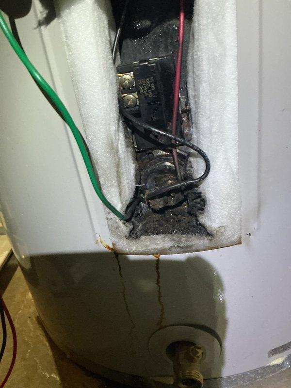 Diagnosed electric water heater with significant corrosion and burn marks at the upper electrical connection compartment. Inspection revealed water leakage into the thermostat area causing electrical damage and terminal deterioration. Replaced damaged thermostat assembly and cleaned corrosion to restore proper operation.