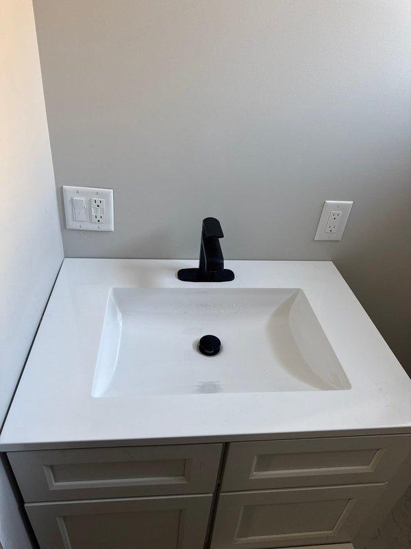 Completed the Mason finishing plumbing project by installing a white porcelain toilet with chrome flush handle and a modern bathroom vanity with rectangular white sink basin featuring black faucet and drain fixtures. All fixtures were properly connected to existing plumbing, tested for leaks, and confirmed to be in good working order with proper drainage.