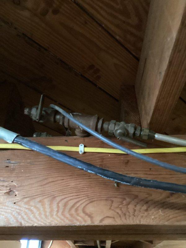 Conducted assessment for water heater replacement in 1940-era single-family home. Existing unit is 86 years old with visible deterioration, installed against brick wall in utility area with outdated insulation strapping and connection points. Inspection of plumbing components revealed aging pipe fittings integrated within wooden structural frame requiring modernization for proper installation compliance. Photos documented current installation configuration and structural considerations for replacement planning.