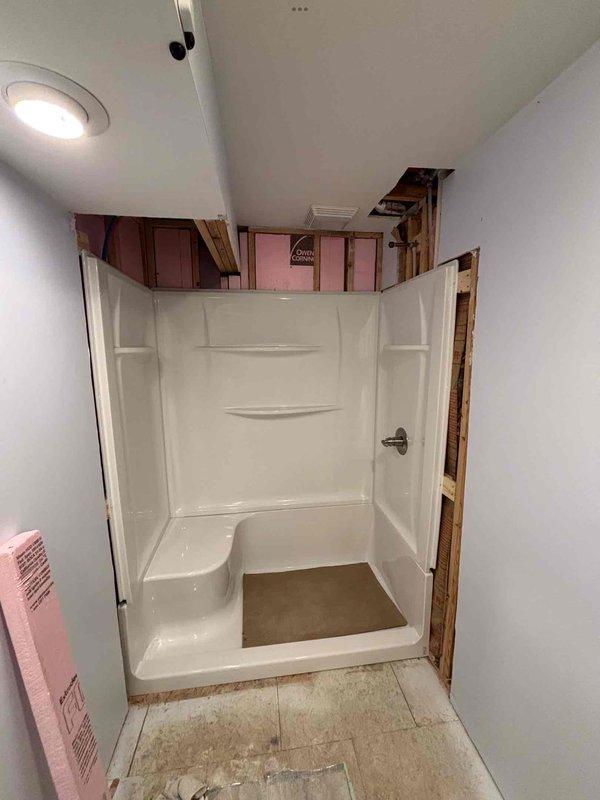 Completed installation of customer-supplied 60"x32" 4-piece shower with right-hand drain. Work included installing new customer-supplied valve, relocating drain (required concrete breaking and finishing), and installing new water piping. Shower unit with built-in shelves and seat was successfully installed while surrounding areas were left prepared for client-responsible work including flooring, drywall, trim, and other bathroom fixtures.