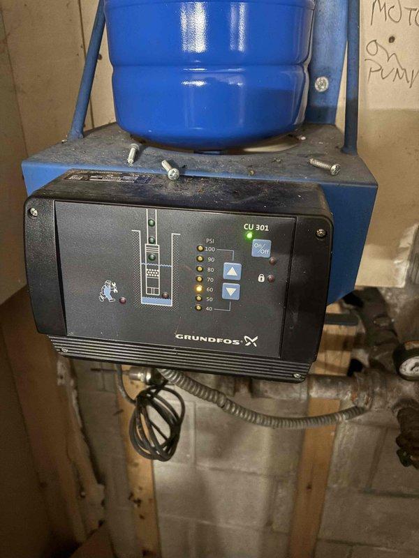 Conducted assessment of existing water system with saturated bladder tank requiring replacement. Documented current installation including Grundfos CU 301 control panel with digital PSI interface (40-100), blue pressure vessel, and associated piping system showing significant rust on joints and connections. System includes pressure gauge and multiple valves mounted on concrete block wall with wooden supports. Replacement recommendation provided to client via CWOW channel.