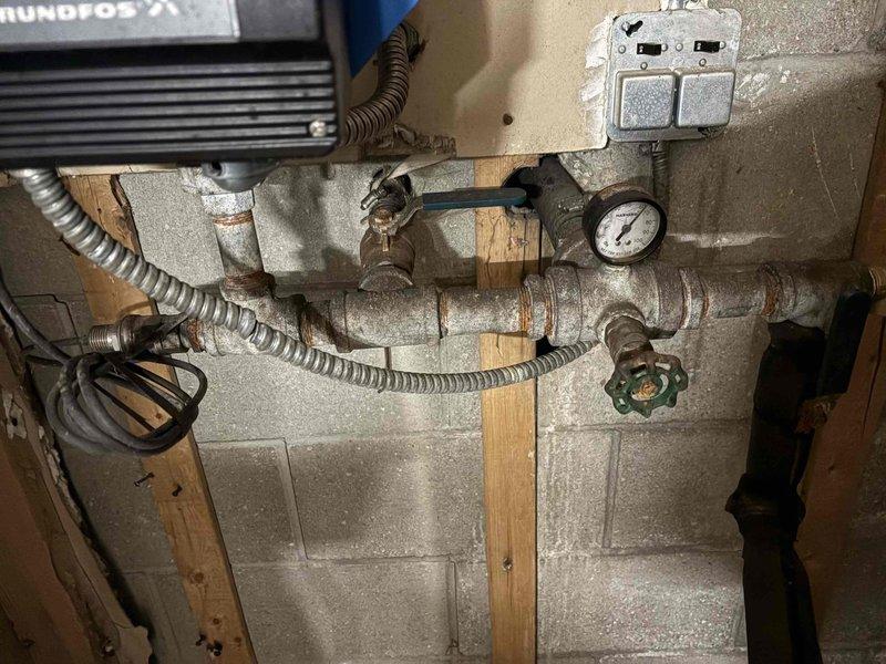 Conducted assessment of existing water system with saturated bladder tank requiring replacement. Documented current installation including Grundfos CU 301 control panel with digital PSI interface (40-100), blue pressure vessel, and associated piping system showing significant rust on joints and connections. System includes pressure gauge and multiple valves mounted on concrete block wall with wooden supports. Replacement recommendation provided to client via CWOW channel.