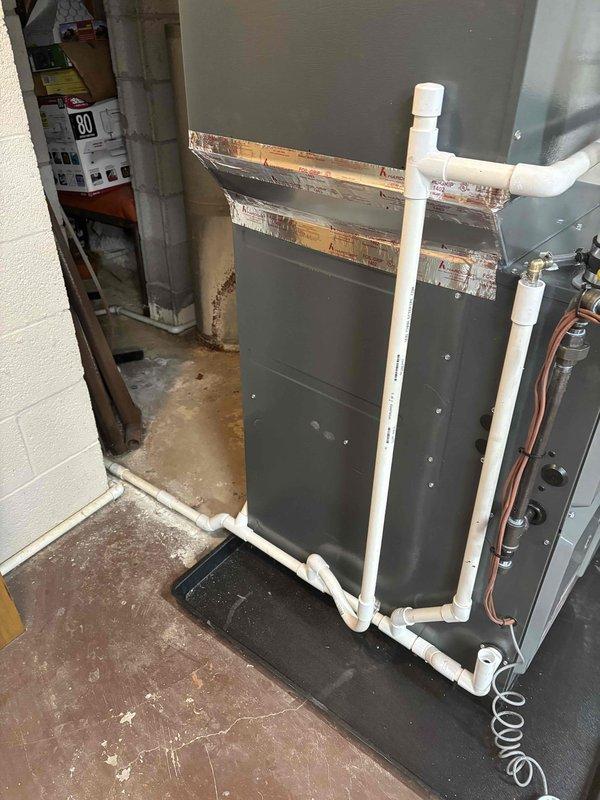 Completed installation of new furnace system with proper condensate drainage setup. Installed white PVC drainage pipes with appropriate elbows and connections to ensure proper water removal. System includes metal cabinet housing with sealed panels and copper line connections mounted on drain pan for added protection.