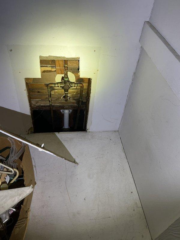 Accessed wall cavity to repair non-functioning shower faucet. Removed rectangular drywall section to expose aged copper piping and valve assembly. Successfully replaced faulty valve, restoring proper shower operation.