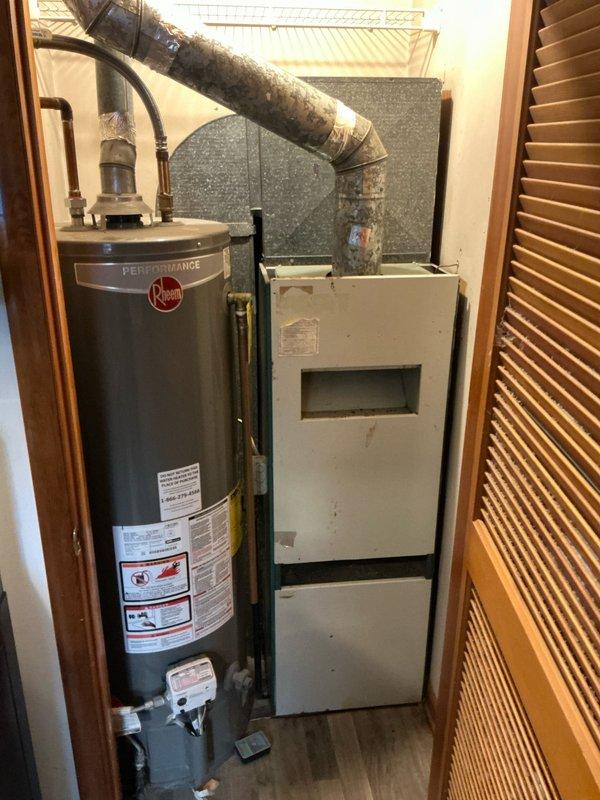 Conducted furnace replacement estimate for a 58-year-old Bard system with customer request for AC attachment. Inspected existing ductwork, noting aged galvanized steel ducts with visible wear at connection joints and previous tape repairs. Evaluated utility closet layout containing a Rheem Performance water heater adjacent to the current HVAC unit, with limited space considerations and insulated ductwork requiring assessment for compatibility with new system.