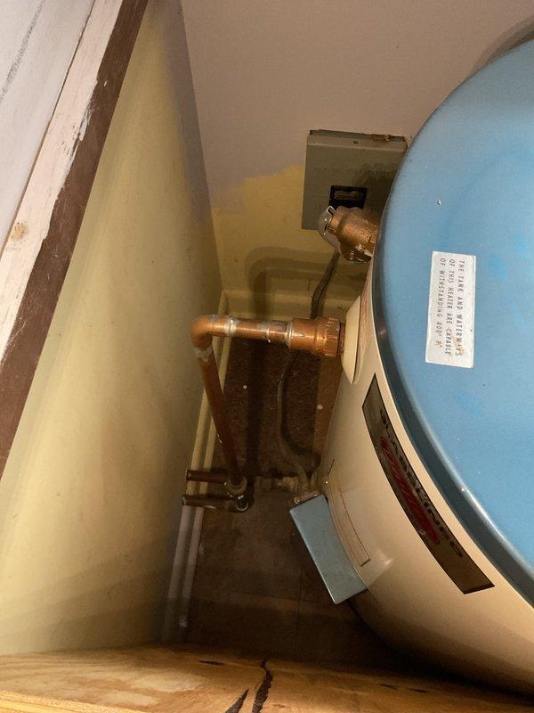 Completed water heater estimate for CWOW customer in confined utility space. Assessed existing aging blue cylindrical water heater with copper piping showing signs of wear and mineral deposits. Evaluated Watts valve system and measured clearances to determine appropriate replacement options considering the limited installation area.