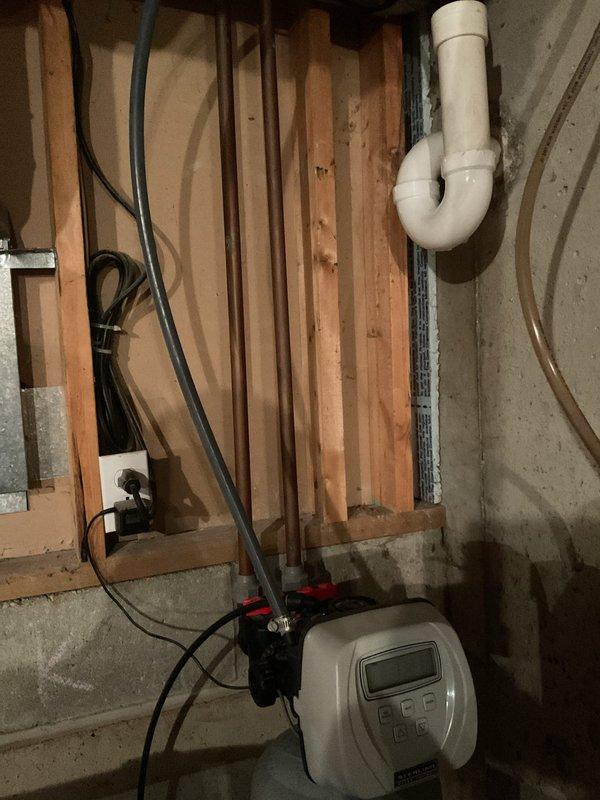 Performed assessment of current water softener system in unfinished basement area for requote. Evaluated existing plumbing infrastructure including PVC drainage pipes, water treatment equipment with digital control panel, and connection points. Customer inquired about previous offer of complimentary toilet arms with new water softener purchase; documented request for inclusion in final estimate.