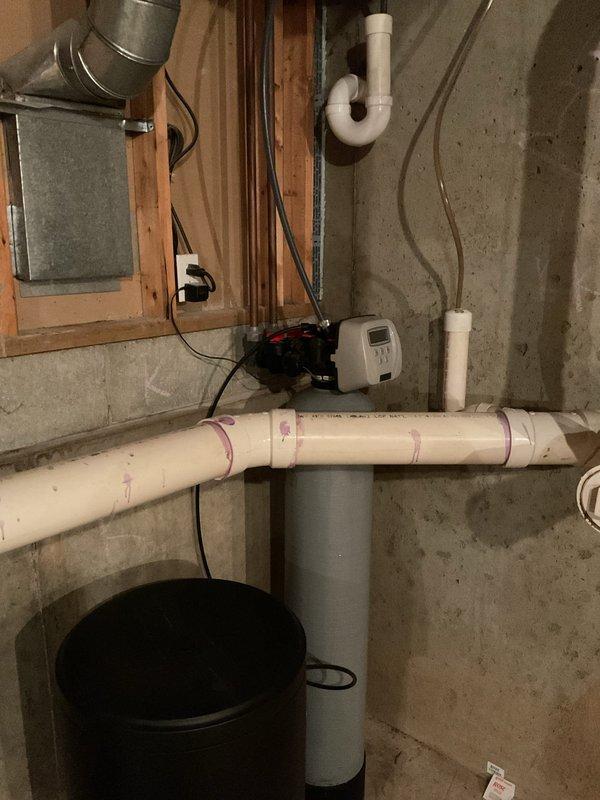 Performed assessment of current water softener system in unfinished basement area for requote. Evaluated existing plumbing infrastructure including PVC drainage pipes, water treatment equipment with digital control panel, and connection points. Customer inquired about previous offer of complimentary toilet arms with new water softener purchase; documented request for inclusion in final estimate.