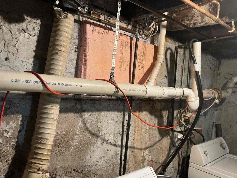 Responded to a main drain backup call. Inspected the plumbing system in the basement area, which included PVC drain pipes with a brass valve showing signs of corrosion. Cleared the blockage in the 3.25" Freedom Flow drain line, restoring proper drainage function.