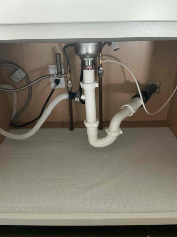 Conducted inspection and installation of new garbage disposal system in 1960s single-family residence. Existing plumbing under sink features standard PVC drain assembly with P-trap configuration and copper supply lines, all in good working condition. Documented current plumbing setup with photos to ensure proper installation compatibility with the home's 60-year-old plumbing infrastructure.